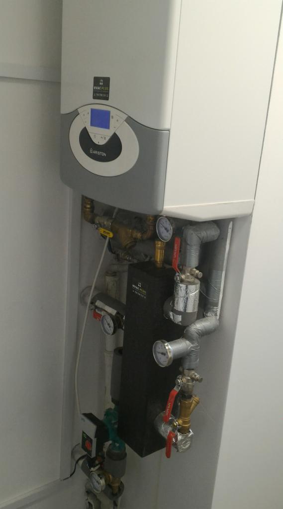 Kocioł gazowy Ariston z podłączonymi rurami i manometrami w białym pomieszczeniu technicznym.