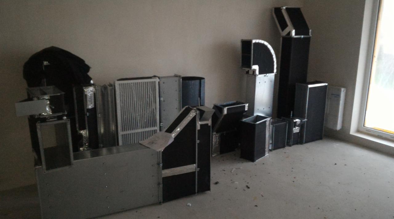 Elementy instalacji wentylacyjnej (kanały, filtry) z metalu i czarnej izolacji, przygotowane do montażu w Chorzowie, widoczne na surowym betonie w pomieszczeniu z oknem.