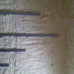 Ściana pokryta warstwą jasnej pianki izolacyjnej z widocznymi, poziomymi profilami montażowymi.