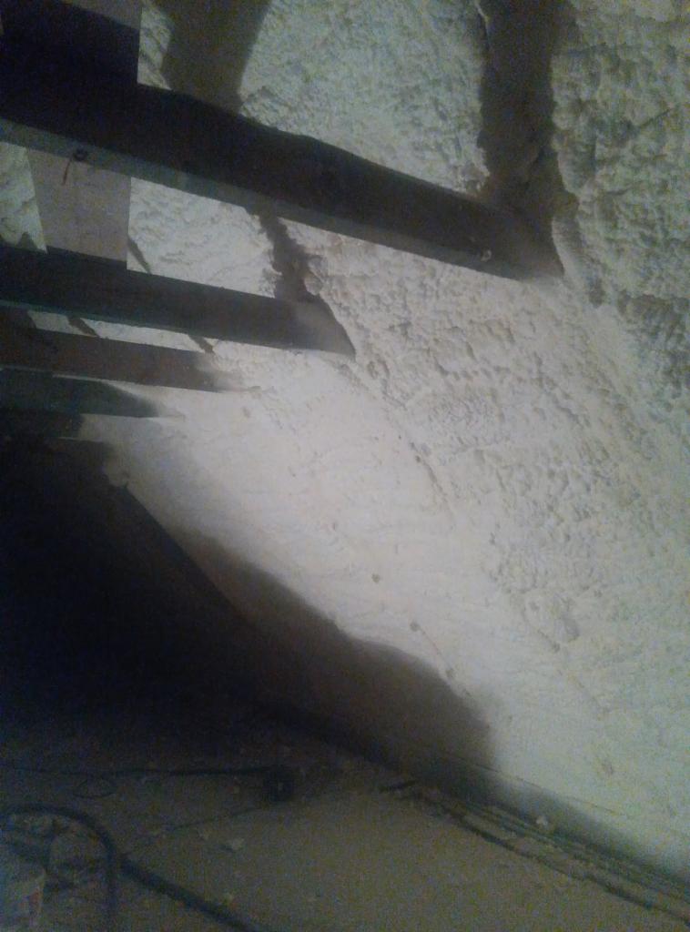 Ściana i strop poddasza po natrysku izolacji piankowej, widoczne drewniane belki stropowe i nierównomierna struktura piany.