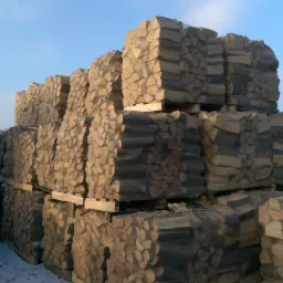 Ułożone palety z pociętym drewnem kominkowym w siatkach, częściowo pokryte śniegiem, widok z placu składowego w Miasteczku Śląskim.