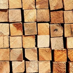 Stos r&oacute;wno ułożonych, przyciętych kwadratowych belek z widocznym rysunkiem słoj&oacute;w drewna i śladami po cięciu.