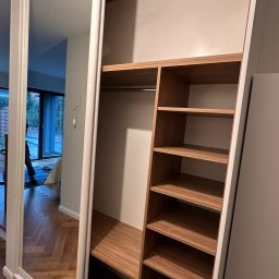 MYSTEK SPÓŁKA Z OGRANICZONĄ ODPOWIEDZIALNOŚCIĄ - Wnętrze szafy wnękowej z lustrzanymi drzwiami przesuwnymi i drewnianymi półkami, widoczne z perspektywy wnętrza garderoby. Uwagę przykuwa minimalistyczny design i dbałość o detale.