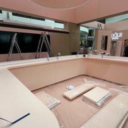 MYSTEK SPÓŁKA Z OGRANICZONĄ ODPOWIEDZIALNOŚCIĄ - Montaż różowej lady recepcyjnej z logo 'Dole Foto' w przestrzeni handlowej. Widoczne elementy konstrukcyjne, drabiny i pracownicy podczas instalacji.