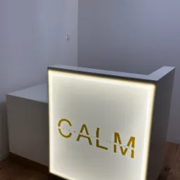 Biała lada recepcyjna z podświetlanym logo 'CALM Gabinet Psychoterapii' na drewnianej podłodze, w minimalistycznym wnętrzu z oświetleniem LED.