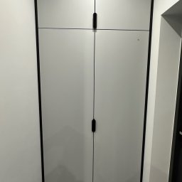 MYSTEK SPÓŁKA Z OGRANICZONĄ ODPOWIEDZIALNOŚCIĄ - Jasnoszara szafa wnękowa z czarnymi detalami i minimalistycznymi uchwytami, wkomponowana w jasne wnętrze, widoczna z perspektywy podłogi.