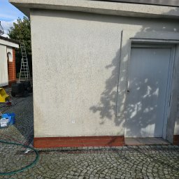 BADI Robert Badecki - Elewacja budynku z szorstkim tynkiem, widoczne ślady po niedawnym czyszczeniu, w tle drabina i urządzenie czyszczące na kółkach, na pierwszym planie kostka brukowa i węże doprowadzające wodę.