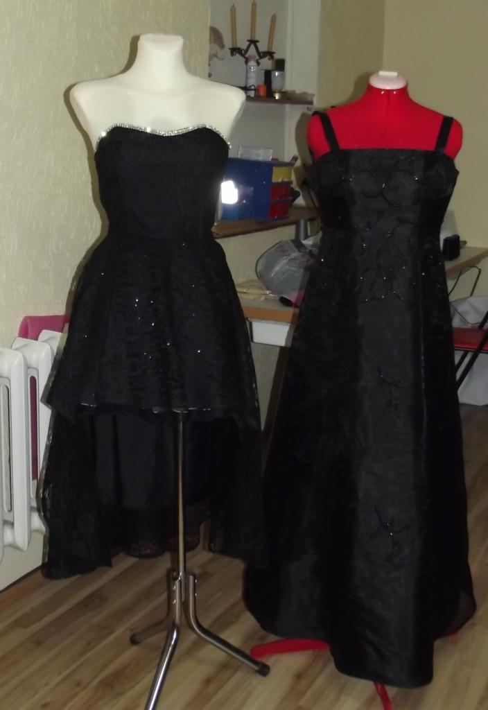 Dwie czarne, wieczorowe suknie na manekinach: asymetryczna z cekinami i kryształkami oraz długa na ramiączkach z delikatnym wzorem, w tle warsztat krawiecki.