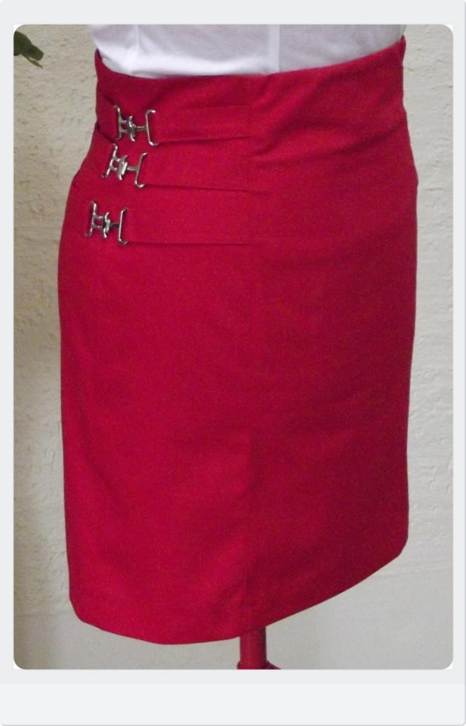 Czerwona spódnica ołówkowa z wysokim stanem i ozdobnymi, metalowymi sprzączkami po lewej stronie, prezentowana na manekinie.