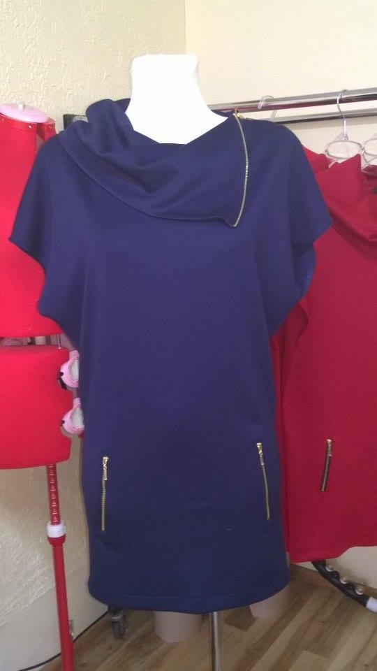 Granatowa sukienka z asymetrycznym dekoltem i złotymi zamkami błyskawicznymi, prezentowana na manekinie obok czerwonego manekina i wiszącej czerwonej sukienki.