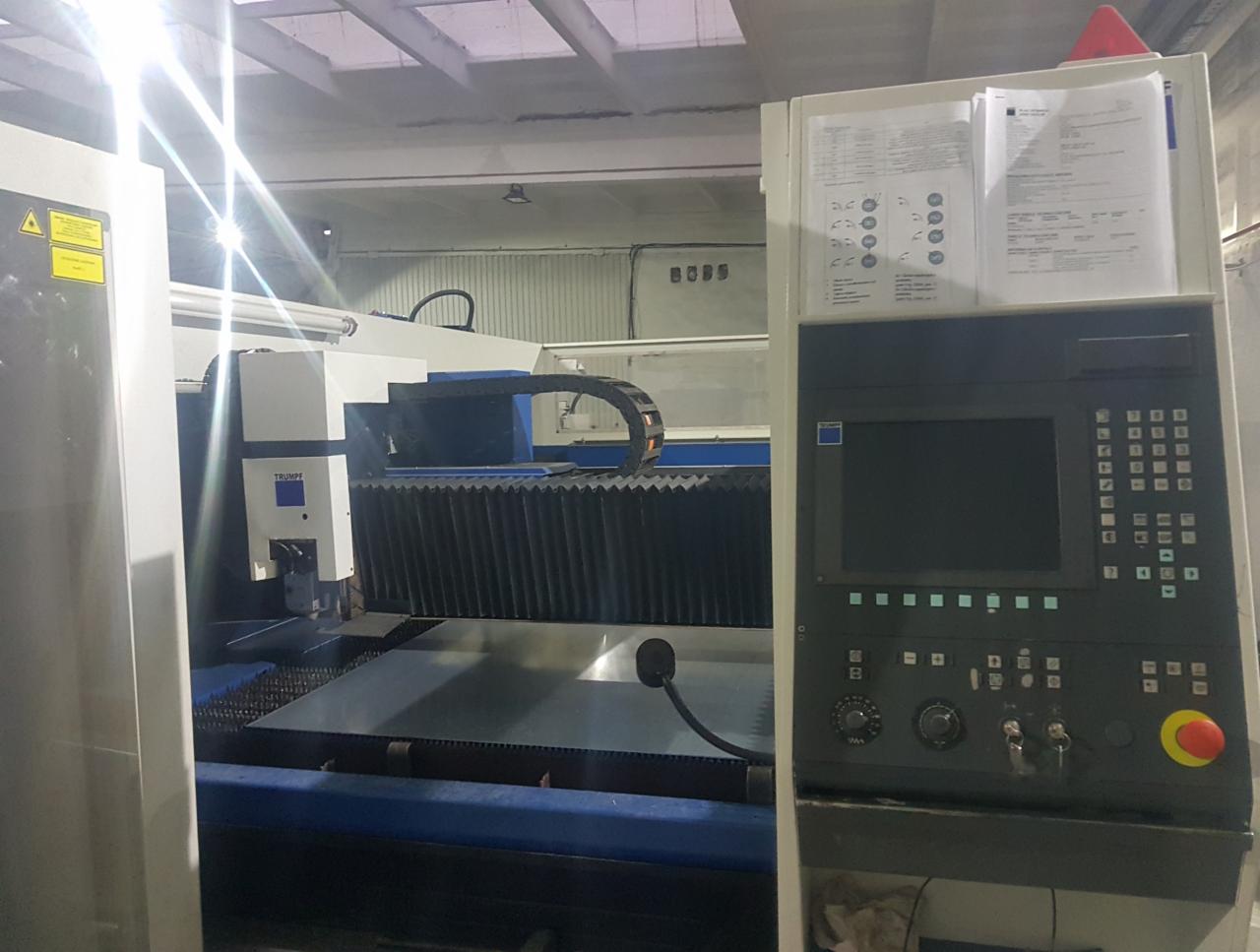 Przemysłowa maszyna do cięcia metali laserem marki Trumpf, widoczny panel sterowania z ekranem i przyciskami, oraz arkusz blachy na stole roboczym.