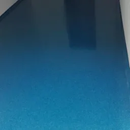 Błyszcząca, turkusowa posadzka z drobnymi ziarnami, wykonana w pustym pomieszczeniu z białymi ścianami i ciemną listwą przypodłogową, widok na otwarte przejście do kolejnego pomieszczenia.