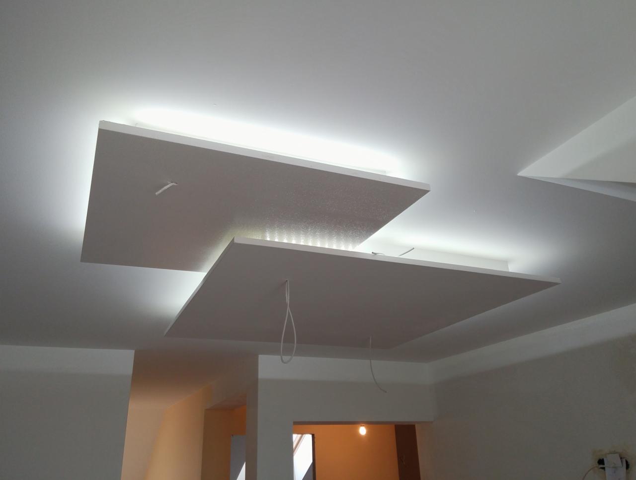 Nowoczesny sufit podwieszany z oświetleniem LED, białe płyty gipsowe tworzące geometryczną kompozycję, widoczne przewody instalacyjne w trakcie montażu.