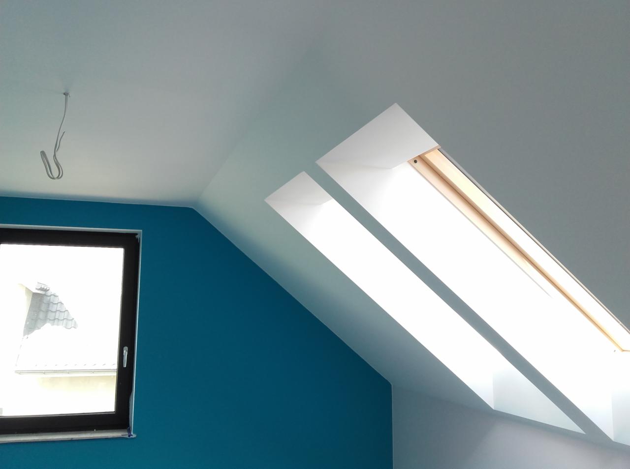 Pomalowane poddasze z oknami dachowymi, ściana w kolorze turkusowym, sufit biały, widoczne zawieszenie na suficie.