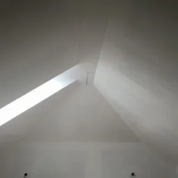 Poddasze po malowaniu na biało, widoczne okno dachowe i delikatne niedoskonałości na ścianie, dwa otwory na dole ściany.