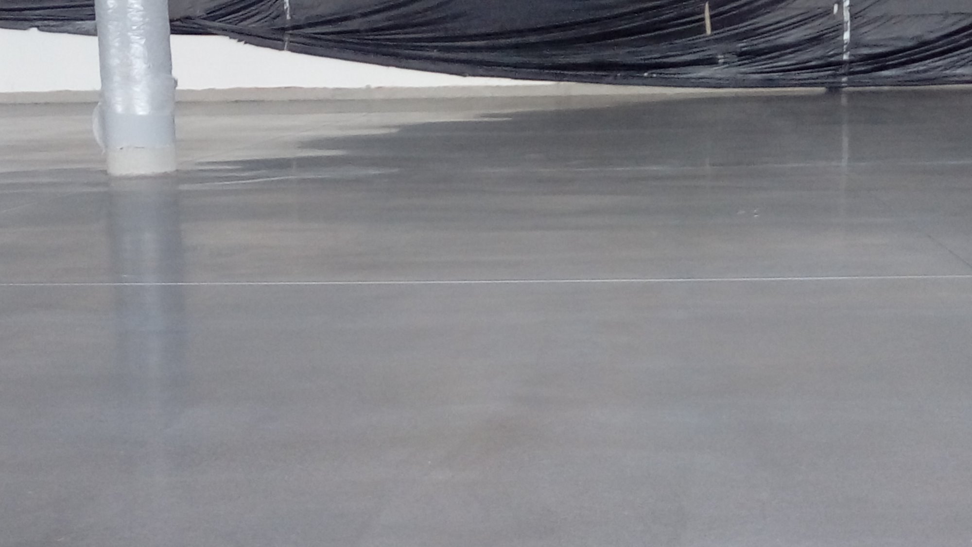 Wypoziomowana, gładka, szara posadzka w hali przemysłowej z widoczną dylatacją i osłoniętym słupem nośnym.