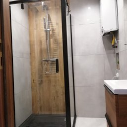 LEVEL - Nowoczesna kabina prysznicowa z czarną ramą i drewnopodobnym panelem ściennym, widoczny fragment umywalki i piec gazowy.