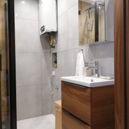 LEVEL - Nowoczesna łazienka z drewnianą szafką pod umywalką, grzejnikiem gazowym z rurą odprowadzającą spaliny oraz lustrem odbijającym kabinę prysznicową.