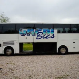 Biały autokar z otwartymi drzwiami i napisem 'Capri Bus' z motywem plaży, stojący na żwirowym parkingu w pochmurny dzień.