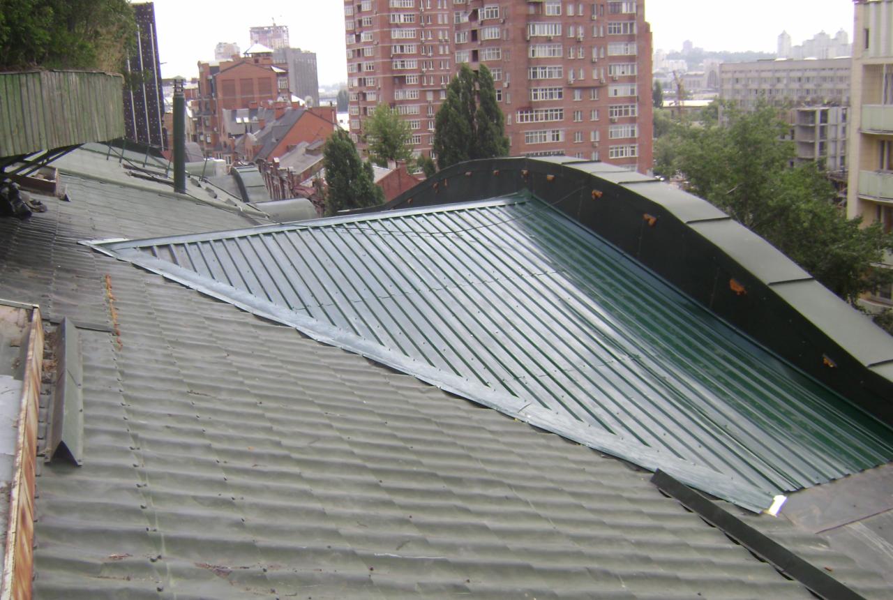 Fragment dachu z blachy trapezowej w Ternopilu, z widocznym połączeniem starego i nowego pokrycia, z budynkami w tle.