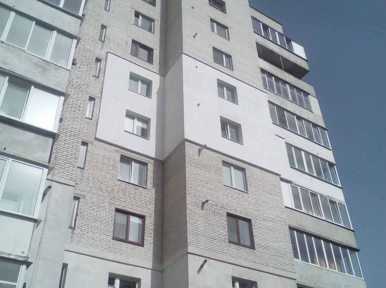 Wielopiętrowy budynek mieszkalny z jasnej cegły z oknami i balkonami, sfotografowany pod kątem od dołu w słoneczny dzień.