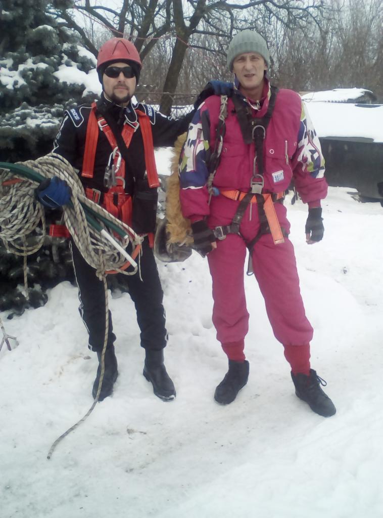Dwóch mężczyzn w odzieży roboczej i uprzężach stoi na śniegu, jeden trzyma zwój lin, prawdopodobnie przed pracą na wysokościach.