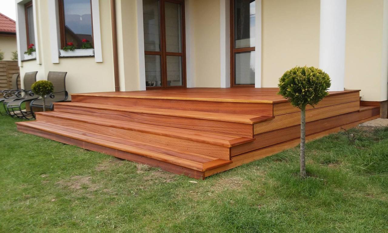 Nowoczesny taras drewniany z wyraźnymi schodami, wykonany w Słubicach, z widoczną strukturą drewna i małym drzewkiem ozdobnym na trawniku.