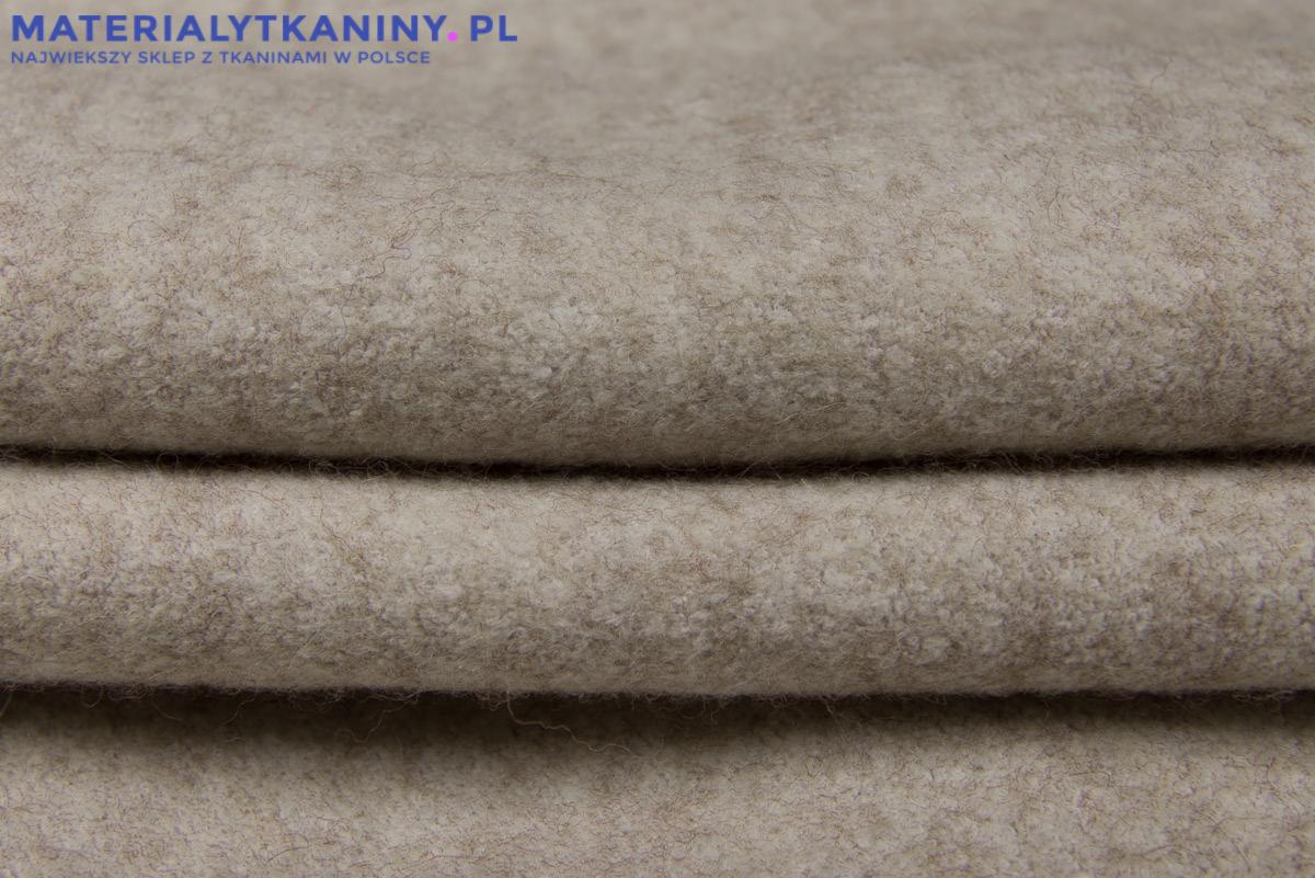Beżowa, gruba tkanina wełniana ułożona w fałdy, widoczna faktura materiału, logo sklepu internetowego w górnym lewym rogu.