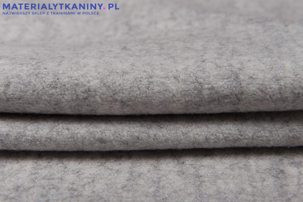 Szary materiał wełniany złożony w fałdy, widoczna faktura tkaniny.