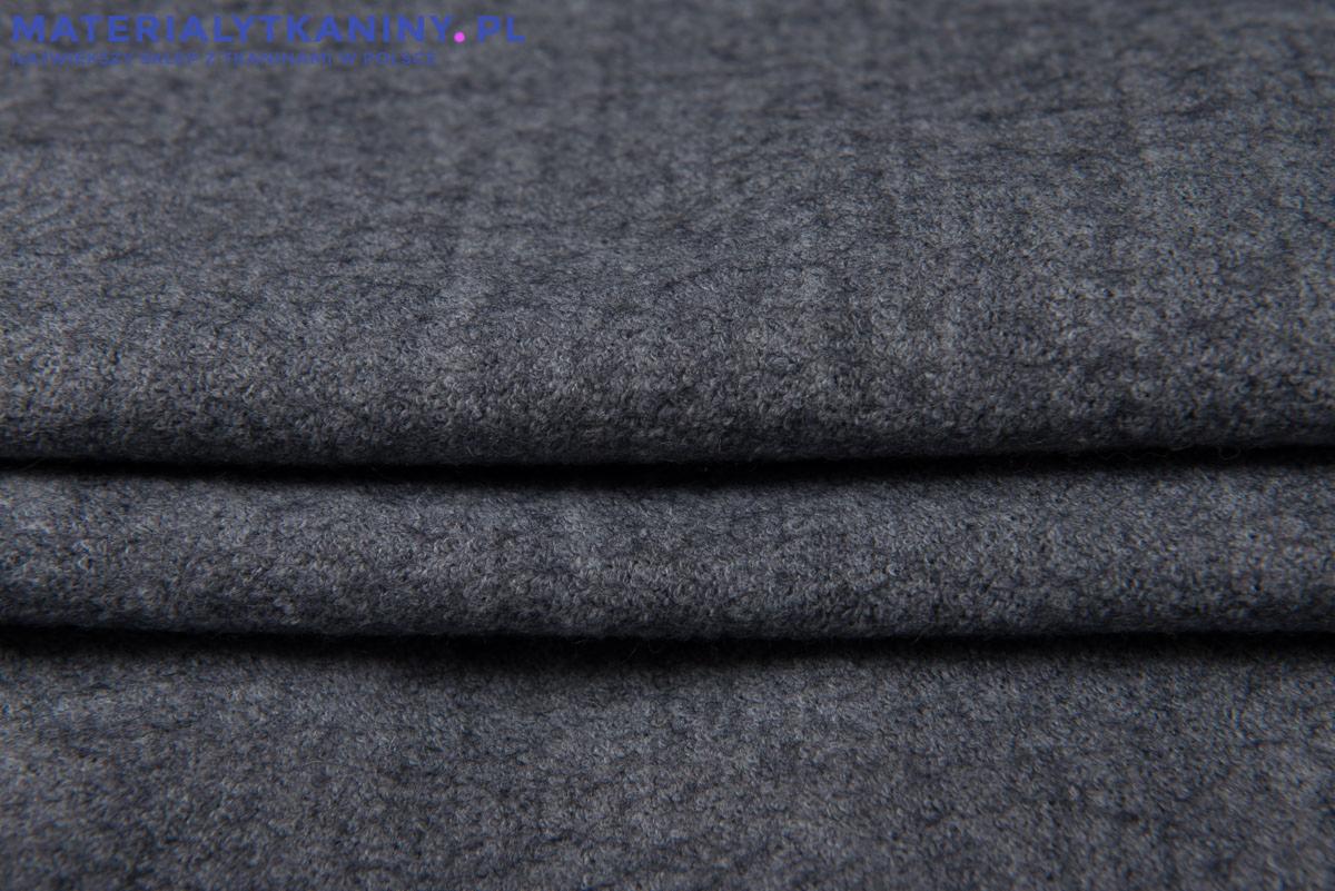 Szczegółowe ujęcie szarej, mięsistej tkaniny wełnianej z widoczną fakturą i delikatnym drapowaniem, prezentujące jakość i strukturę materiału.