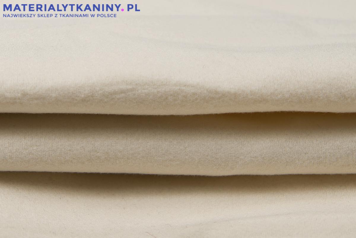 Kremowa, gruba tkanina wełniana ułożona w fałdy, widoczne logo sklepu internetowego z tkaninami w górnej części kadru.