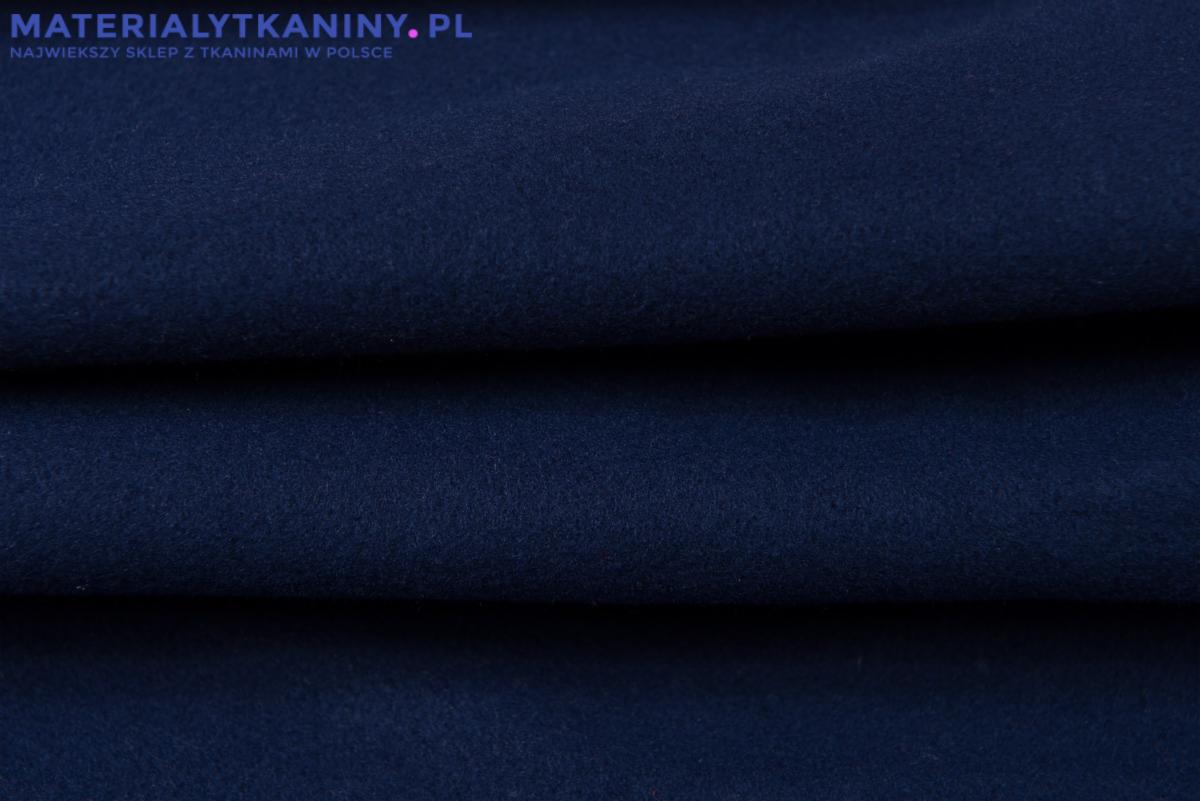 Zbliżenie na granatową, miękką tkaninę z delikatnym meszkiem, ułożoną w fałdy, z widoczną fakturą materiału.