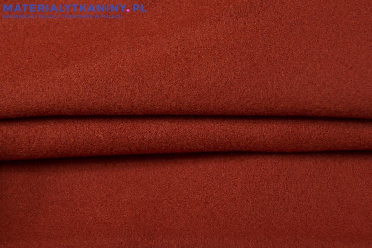 Czerwono-brązowa tkanina wełniana o wyraźnej fakturze, lekko pofałdowana, z widocznym adresem strony internetowej w górnej części kadru.