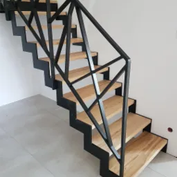 Nowoczesne schody z drewnianymi stopniami i czarną, geometryczną balustradą metalową, widok z dołu.