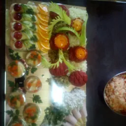 Dekoracyjna taca cateringowa z przekąskami: roladki z szynki z kremem, galaretki z warzywami, pomarańcze w plasterkach, koreczki z pomidorkami cherry i ogórkiem, oraz dekoracje z warzyw i past.