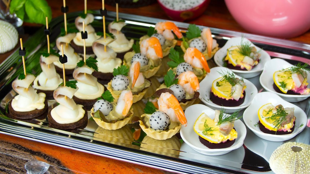 Elegancko podane przekąski na srebrnej tacy: śledzie na ciemnym pieczywie z jajkiem i wykałaczką, tartaletki z krewetkami i smoczym owocem, oraz mini sałatki śledziowe z burakiem i cytryną...