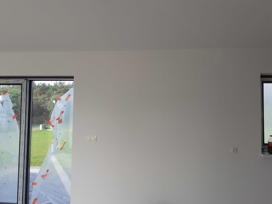 Wnętrze po świeżym malowaniu, okna zabezpieczone folią malarską, widoczne puszki elektryczne.