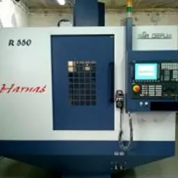 Maszyna CNC z zamkniętą obudową ochronną, widoczny panel sterowania z ekranem i przyciskami, oświetlenie ostrzegawcze na górze, napis 'Harnas' na obudowie.