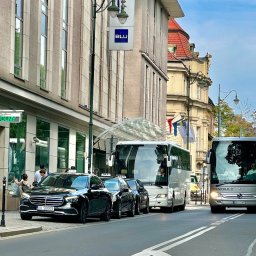 NEED NOW ADRIAN JASKÓLSKI - Czarne taksówki Mercedes i białe autokary stojące przed budynkiem Radisson Blu, widok z poziomu ulicy.