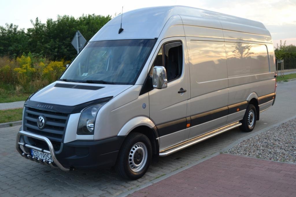 Srebrny Volkswagen Crafter z orurowaniem ochronnym, zaparkowany na kostce brukowej, z widocznymi odbiciami nieba w karoserii i rejestracją ZSD 19054.