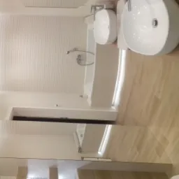 Nowoczesna łazienka z dwoma okrągłymi umywalkami nablatowymi, jasnymi płytkami na ścianach i podłodze oraz minimalistyczną armaturą.