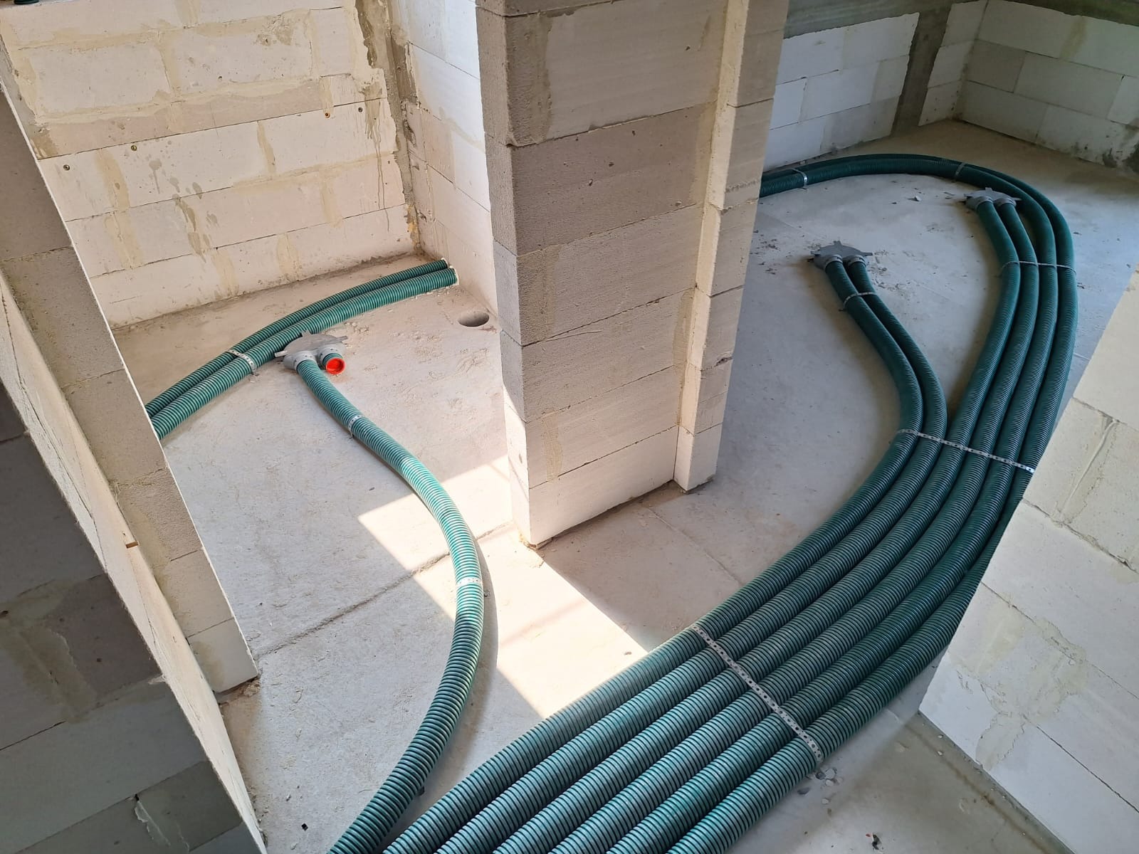 Zielone, karbowane rury wentylacyjne ułożone na surowym betonie wewnątrz budynku z pustaków, widoczne elementy montażowe.