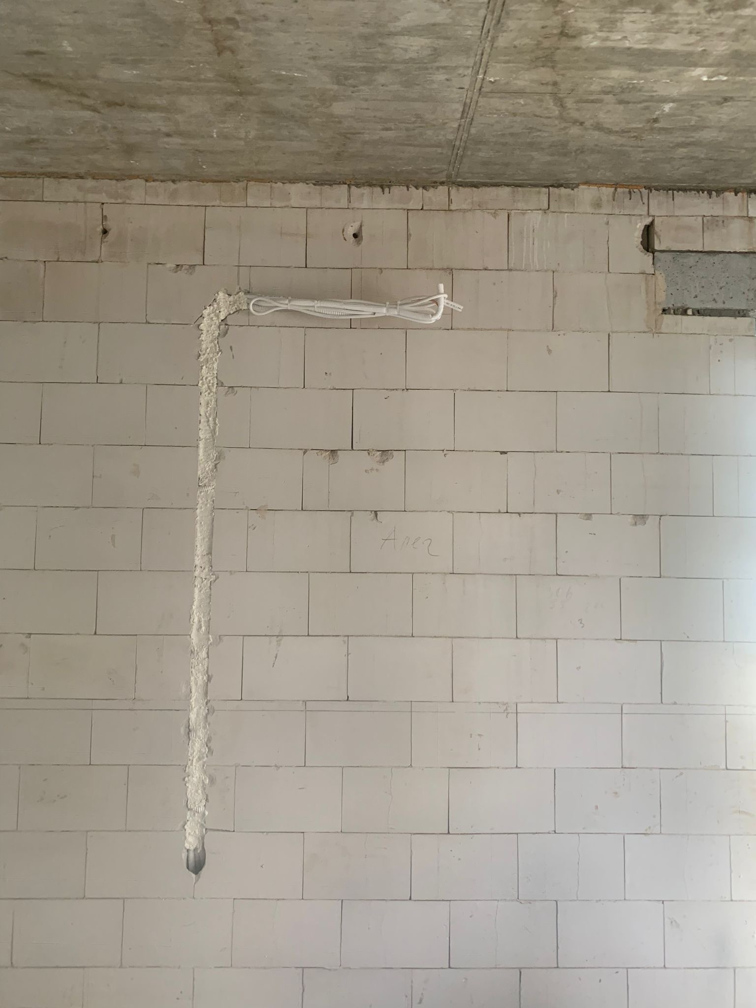 Biała ściana z betonu komórkowego z wyfrezowanym pionowym rowkiem wypełnionym gipsem, w którym umieszczono przewody elektryczne w Łomiankach. Widoczny surowy betonowy sufit.