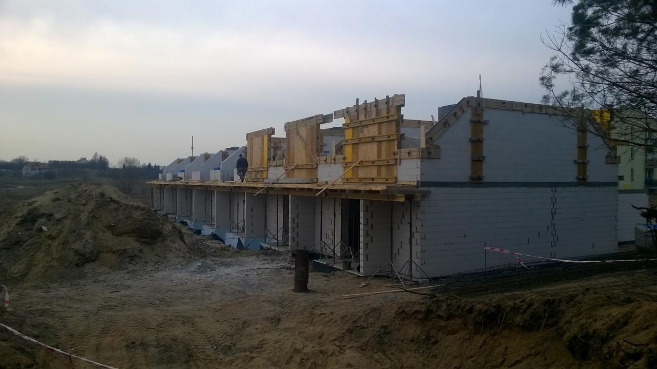 Budowa szeregu domów z betonu komórkowego, widoczne szalunki i zbrojenia, teren budowy z hałdą ziemi.
