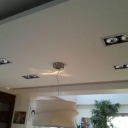 Biały sufit z zamontowanymi czterema parami halogenowych opraw oświetleniowych, w tle widoczny duży, designerski żyrandol.