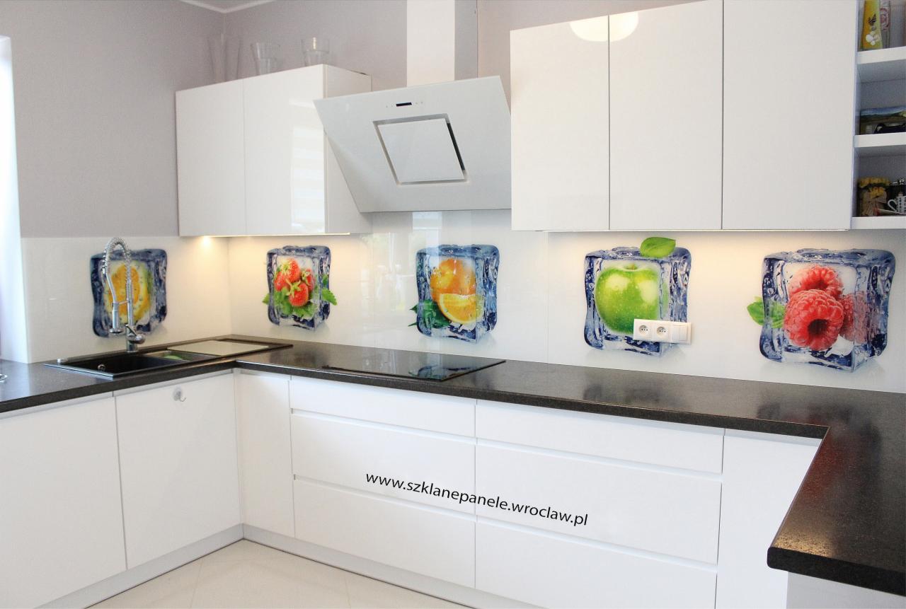 Biała kuchnia z panelami szklanymi przedstawiającymi owoce w kostkach lodu, czarny blat, minimalistyczny okap i szafki bez uchwytów.