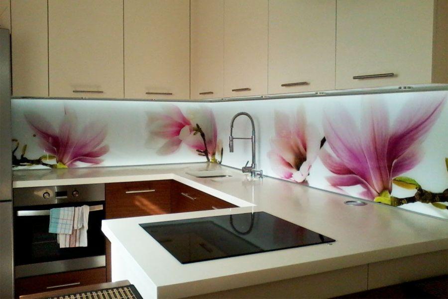 Nowoczesna kuchnia z białymi szafkami i szklanym panelem ściennym z motywem magnolii, oświetlonym od tyłu, oraz indukcyjną płytą grzewczą.