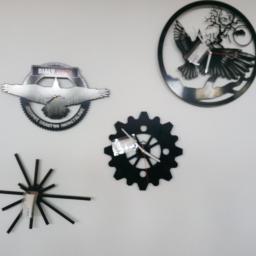 Lizard Waterjet24 - Dekoracyjne, metalowe zegary ścienne o różnych wzorach: orzeł w locie z napisem 'Biały', ptak w okręgu z motywem roślinnym, zębatka oraz abstrakcyjna kompozycja z promieniami.