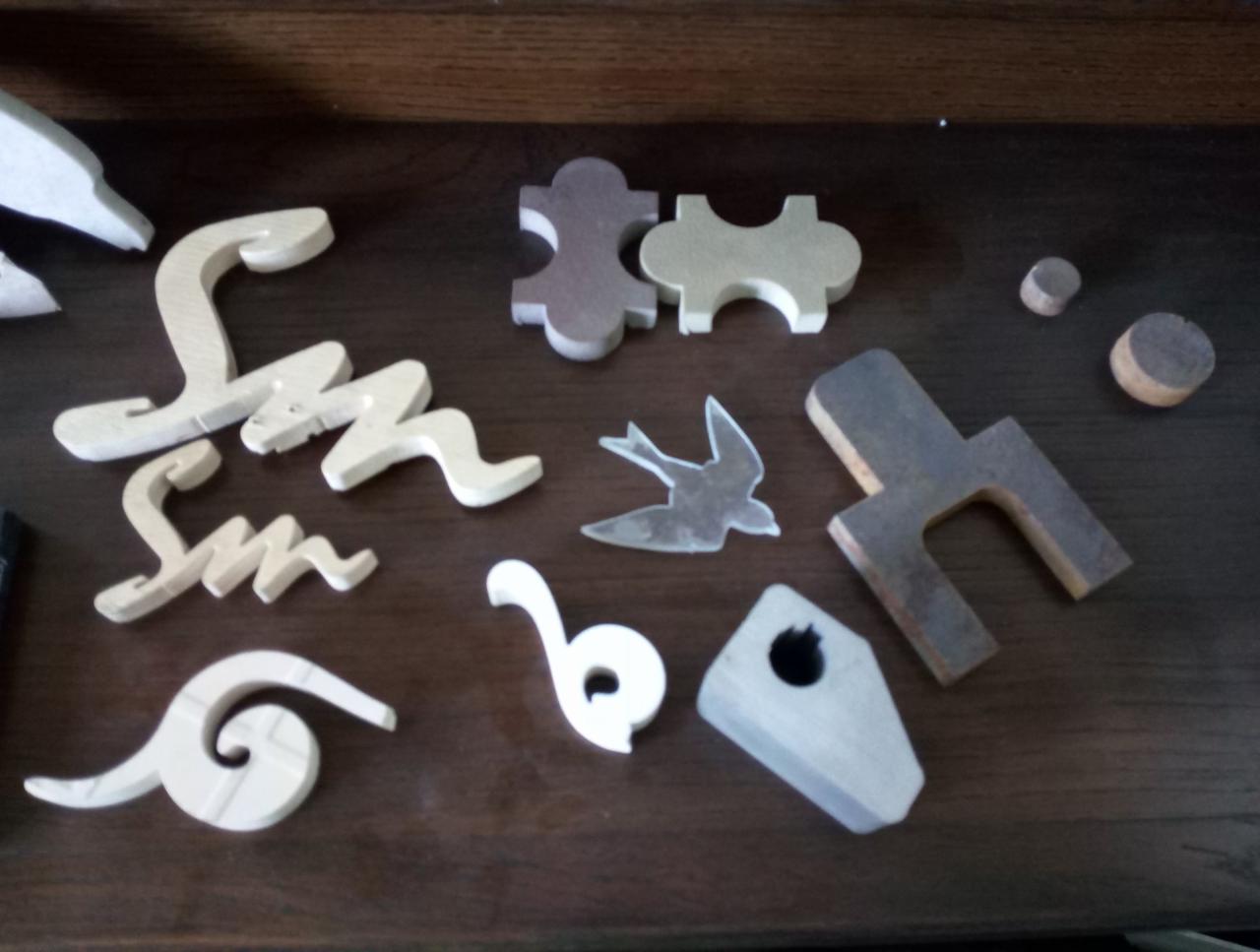 Drewniane elementy dekoracyjne o różnych kształtach i rozmiarach, w tym litery, ptak, puzzle i inne, rozłożone na ciemnej, drewnianej powierzchni.