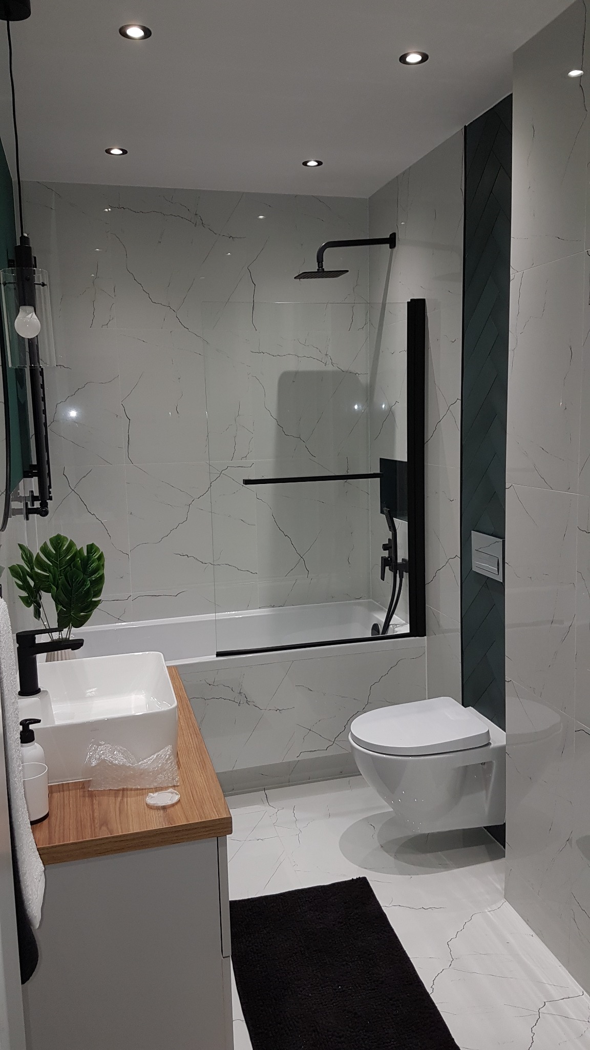 Nowoczesna łazienka z biało-szarymi płytkami imitującymi marmur, czarną armaturą, wiszącą toaletą i umywalką nablatową na drewnianym blacie.